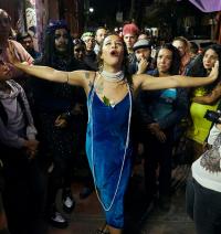 Image of Lía García dressed in a blue dress, arms outstretched toward a crowd on the street