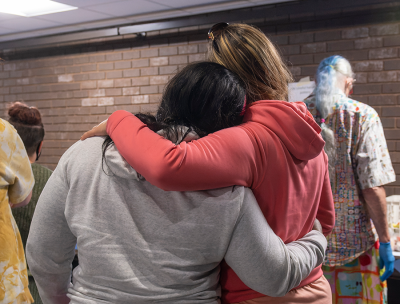 Student in gray sweatshirt and student in pink sweatshirt standing in supportive embrace
