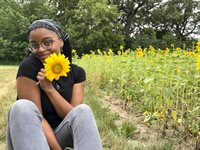 Headshot of HIA scholar Maya Robinson, outdoors holding a yellow flower